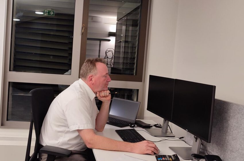 Clark sitzt gelangweilt am Schreibtisch vor abgeschalteten Bildschirmen.